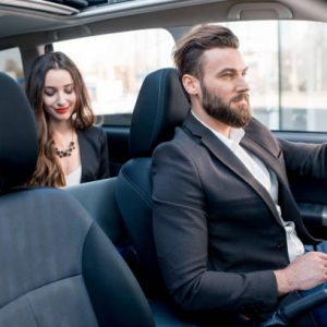 Beautiful businesswoman sitting on the backseat with elegant man driving the car in the city